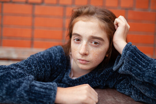 Freckled face teenager in blue sweater at table by brick wall