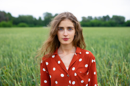 Smiling woman with curly hair in red blouse standing in wheat field