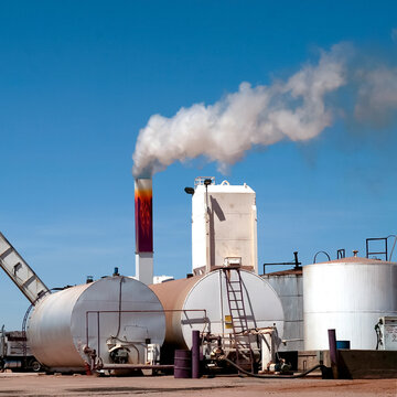 Industrial Facility with Storage Tanks and Smoke Stack Emissions Against Blue Sky