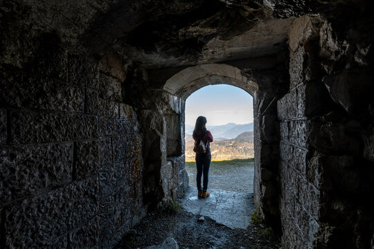 Travel, tourism: Woman looks at mountain landscape from stone archway, exploration, First World war,Cherle Fort,Trentino,Italy.