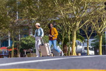 Pair walking plaza pulling beige and silver cases checking phone holding coffee with crossbody bag © wavebreak3