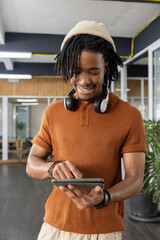 African American man smiling and using tablet inside modern office wearing headphones and rust polo © wavebreak3