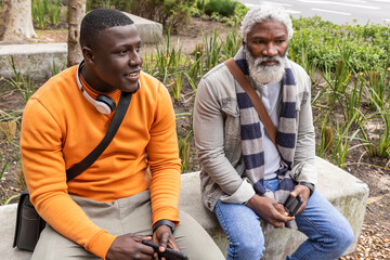 African American male friends sitting on concrete bench at plaza in orange sweater holding phone © wavebreak3