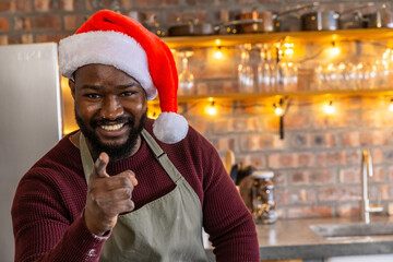 African American man wearing Santa hat and green apron pointing toward you in festive cafe smiling © wavebreak3