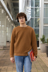 Man standing holding red notebook beneath metal beams by glass facade, wearing headphones © wavebreak3