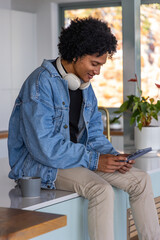 African American man sitting on kitchen counter in denim jacket using tablet with headphones © wavebreak3