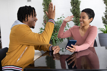 African American couple high-fiving at patio, phone on table, plants behind, wearing casual clothes © wavebreak3