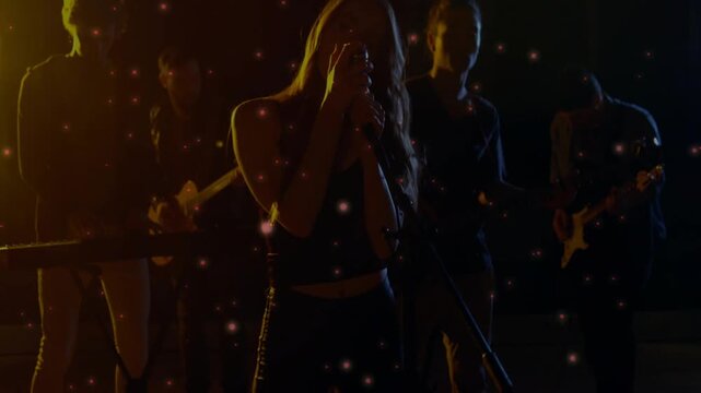 Band performing, lead singer wearing black crop top, shiny pants, singing into mic with guitars