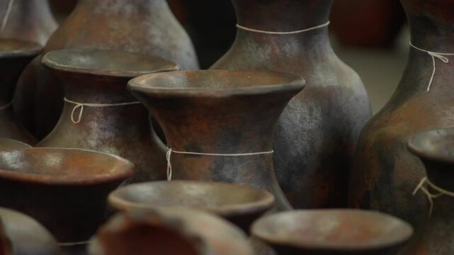 Rustic handmade clay pottery vases and ceramic vessels displayed at Mexican artisan market, shadows of people in backdrop