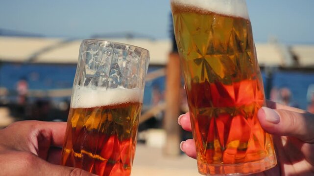Group of friends on vacation celebrating vacation, raising cheers glasses of beer against the backdrop of the sea and beach.