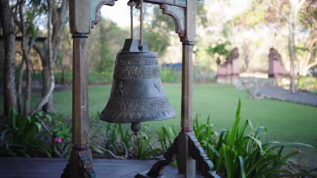 A hanging metal bell displayed on a wooden stand in a veranda setting. Rustic textures and natural lighting create a calm decorative scene with traditional charm and peaceful ambiance.