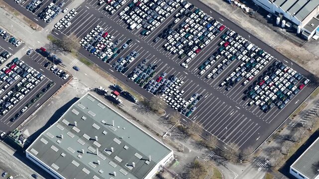 Aerial view of neatly arranged rows of cars filling parking lots next to industrial buildings, creating a pattern of gray and white, Sausheim, Grand Est, France.