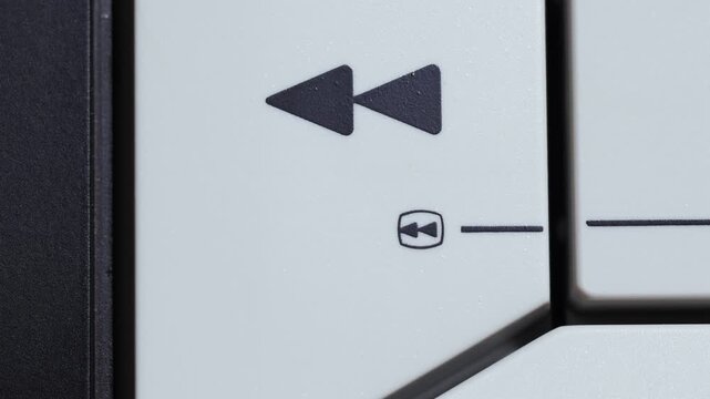 Finger presses white rewind button with black icon on vintage video controller