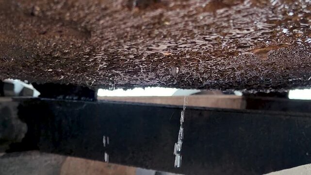 Rusty metal surface dripping water drops from edge, showing corrosion, leak and moisture damage in industrial setting, ideal for grunge texture, decay, environment and background use.