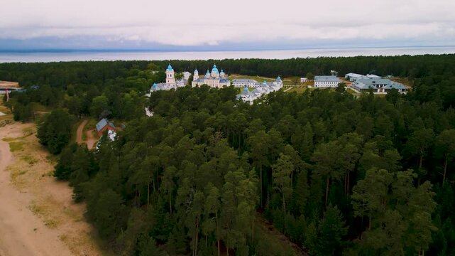 Isolated traditional monastery complex with church blue domes in green forest aerial view.
