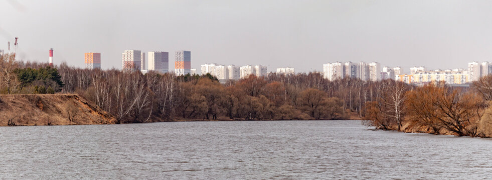 Scenic spring landscape in Strogino with Moskva River bend and residential district of Mitino on the horizon. Wide river view with bare trees and urban skyscrapers under a cloudy April sky. Russia.