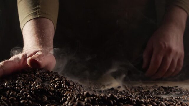 Concept of Coffee production industry. Close-up of barista hands holds hot roasted fresh brown beans on table