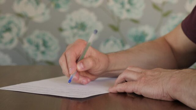 Close-up of a person's hands writing with a blue ballpoint pen on a blank white sheet of paper