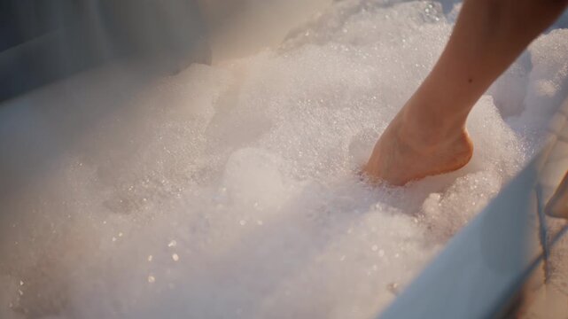 Girl dipping leg foamy bath closeup. Bathroom lady touching foam bathing bubbles