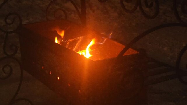 Burning firewood flames in a metal brazier at night