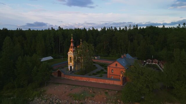 Aerial pull-away shot of a lonely Orthodox church in the deep forest. Wide view of lake horizon and green landscape. 4K drone video.