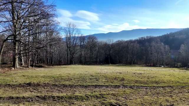 Weathered wooden fence post with a half-round top stands firmly in a sunlit rural field, offering a sense of boundary and natural beauty against distant mountains