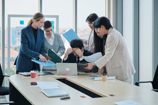 Male company boss is overwhelmed with marketing coworkers, busy document work decisions, stress, and burnout from leader task pressure, meetings at business firm, and multiracial corporate people.