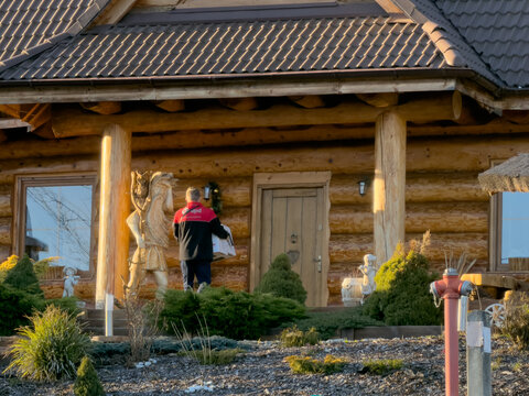 Szklarska Poreba, Poland - December 17, 2025: DPD delivery person brings parcels to a rustic log house, showcasing modern efficient logistics and home delivery