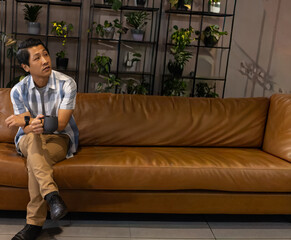Man holding dark mug and gazing upward on sofa, imagining interior design with shelving and plants © wavebreak3