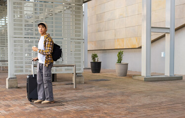 Traveler pausing on plaza waiting for ride, holding cup and suitcase, transit map overlaying scene © wavebreak3