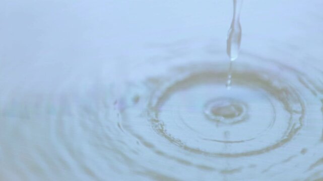Thin stream narrowing, making droplets form, fall, splash and create ripples to show fluid motion