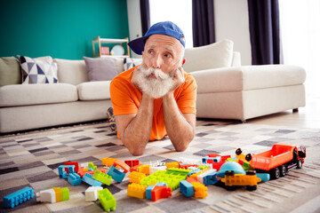 Funny grandpa relaxes on a rug with colorful lego blocks and trucks in a bright cozy living room for a playful weekend indoors © deagreez