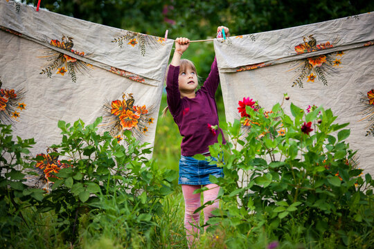 Young girl hanging laundry on a clothesline in a garden, surrounded by greenery and flowers, everyday rural life scene.