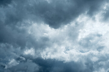 Fototapeta premium A moody and atmospheric sky filled with dense, layered clouds in shades of deep blue, grey, and white. The soft textures and dramatic interplay of light and shadow create a sense of depth and movement
