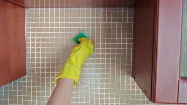 Cleaning tile surface with sponge and gloves in kitchen setting
