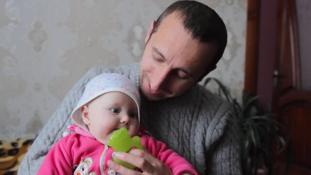 young father gives baby a rubber teether toy, Father helps baby with teething by giving rubber toy