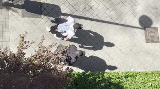 Dos personas con gorra y sombra larga andando vistas desde arriba a vista de p&aacute;jaro 