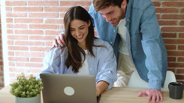 A Happy Couple Laughing and Working Together on a Laptop in Their Modern Home Office