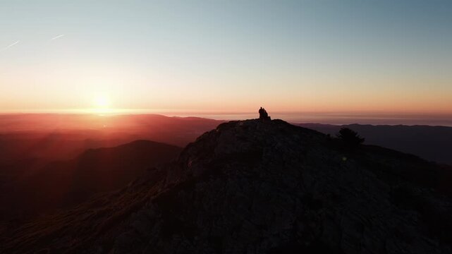 Drone approaches hikers silhouettes at sunrise on Tur&oacute; de l&rsquo;Home Montseny summit