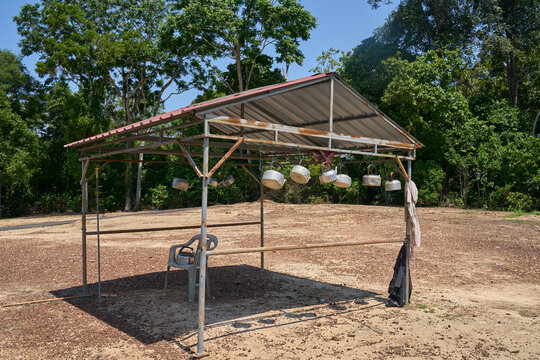 A creative art installation featuring various brightly aluminium kettles and teapots hanging from a wire  under zink roof against green forest background.
