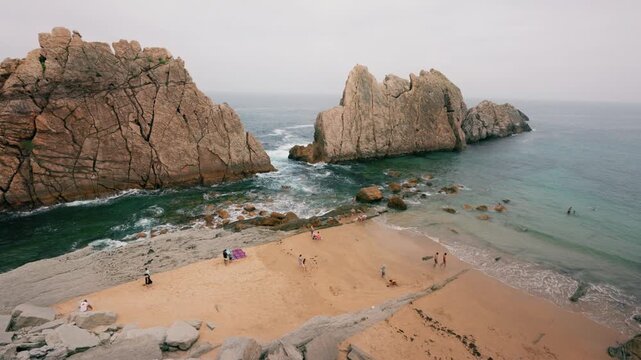 Static shot of La Arn&iacute;a Beach with flysch rock formations, waves and people on sandy shore.