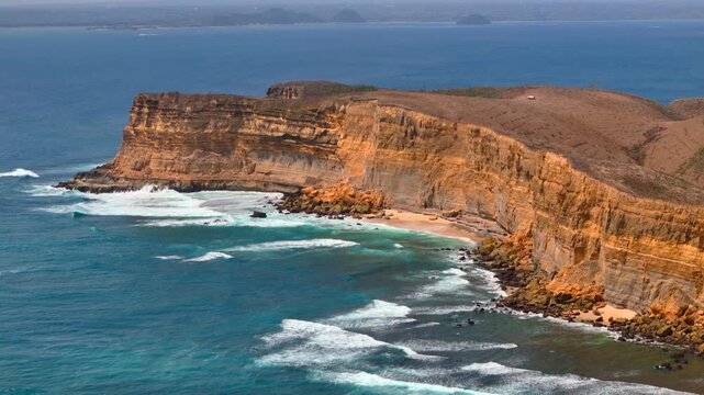Aerial video of layered coastal cliffs with turquoise water white surf hidden sandy coves and rugged tropical shoreline dramatic seascape in bright daylight vivid colors and geological detail