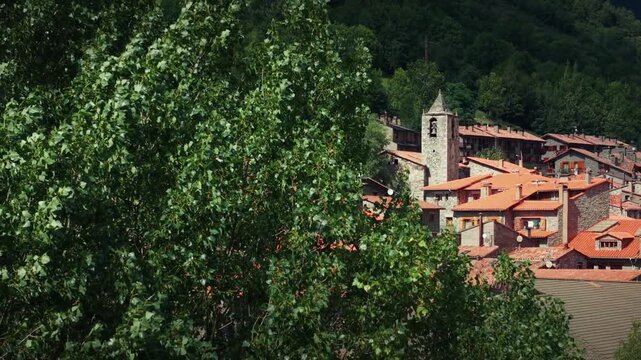 Drone panning reveals Setcases mountain village behind trees with traditional houses and church tower in Catalonia