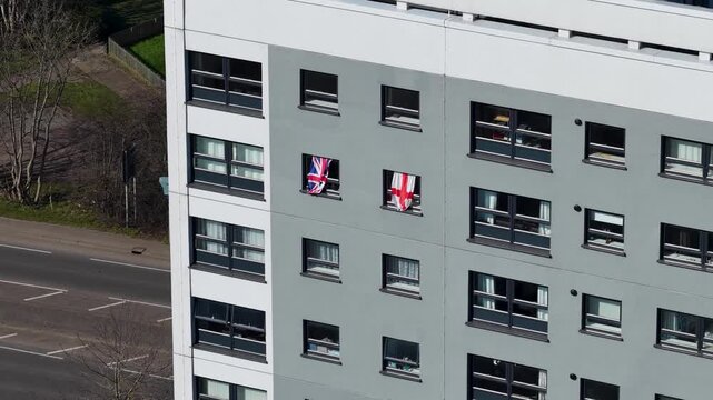 Aerial close view in the town of Seacroft in Leeds showing a tower block facade with England and British St George flags that are hanging out of an apartment window in the spring time