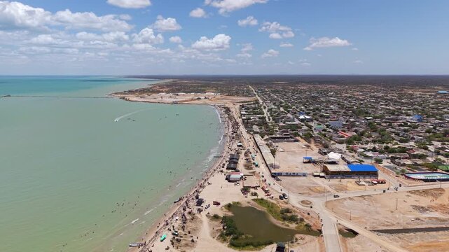 Drone video captures Manaure's stunning coastline with turquoise waters, bustling beaches, and clear skies. Perfect for showcasing Colombia's vibrant seaside atmosphere.