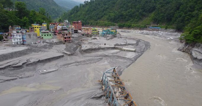 Aerial view of the destructive aftermath of the Melamchi river flood with silt and debris covering the landscape and isolated homes in a vulnerable mountain community in Nepal.