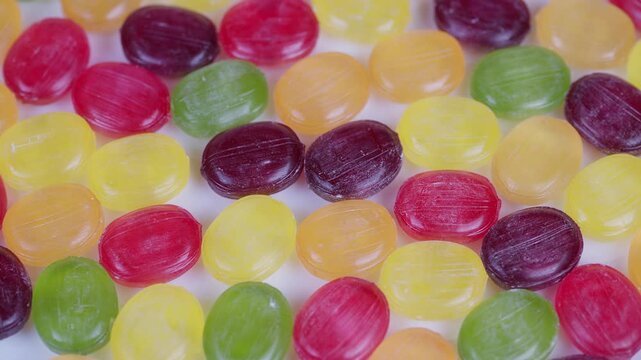 Vibrant sweets with glossy finish. Brightly colored hard candies with shiny glaze in pattern. Closeup of multicolored glossy candies filling frame with textured details