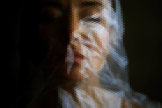 Abstract portrait of a woman with closed eyes behind textured plastic