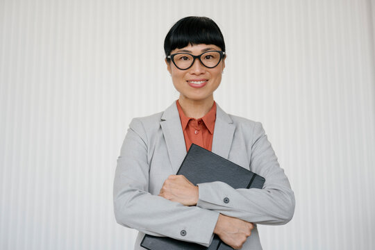 Smiling businesswoman with glasses holding folders in modern office