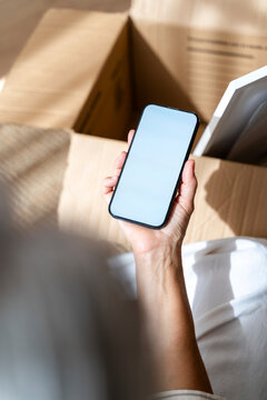 Hand holding smartphone with blank screen at home indoors